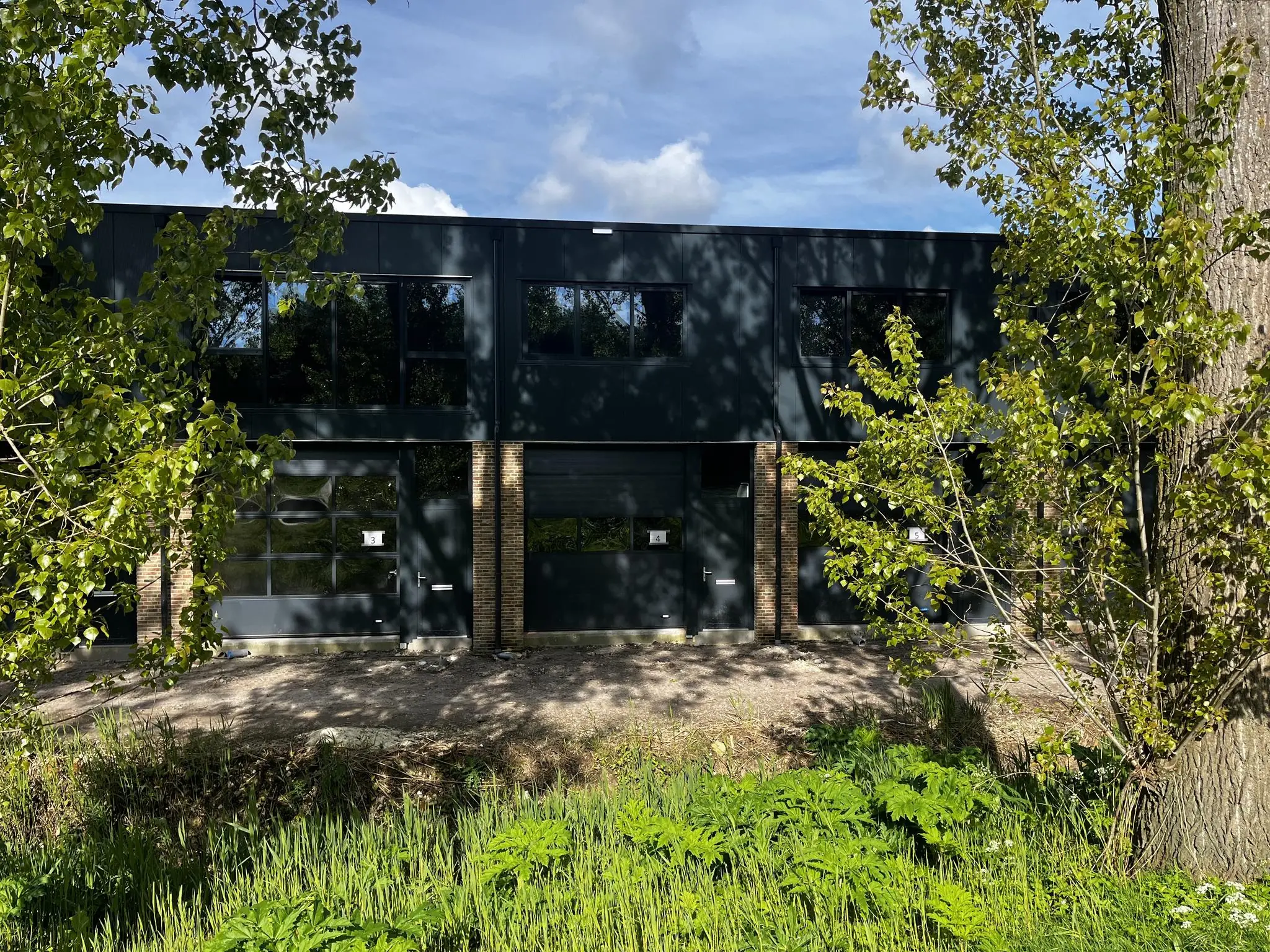 Voorgevel van een modern bedrijfsgebouw aan de Broekdijk West 19-4, omgeven door groene bomen en struiken.
